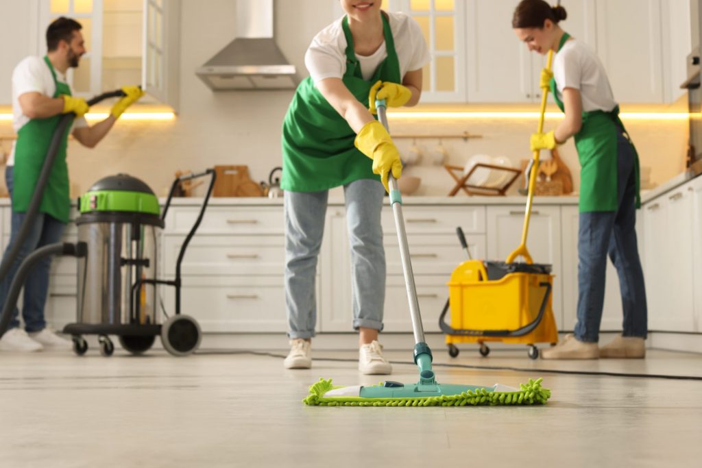 Tres personas con delantales verdes limpian una cocina